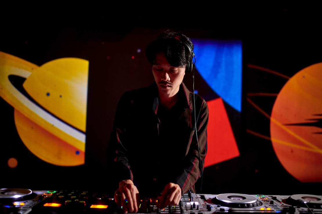 A DJ at the decks in front of a planet projection