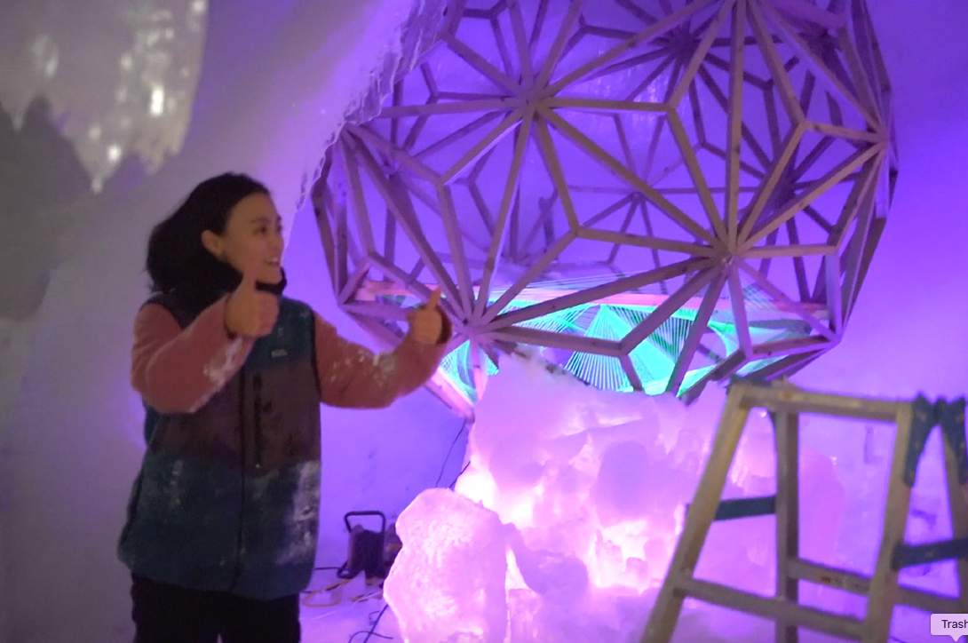 A person at a faceted geometric ice installation lit in purple and pink