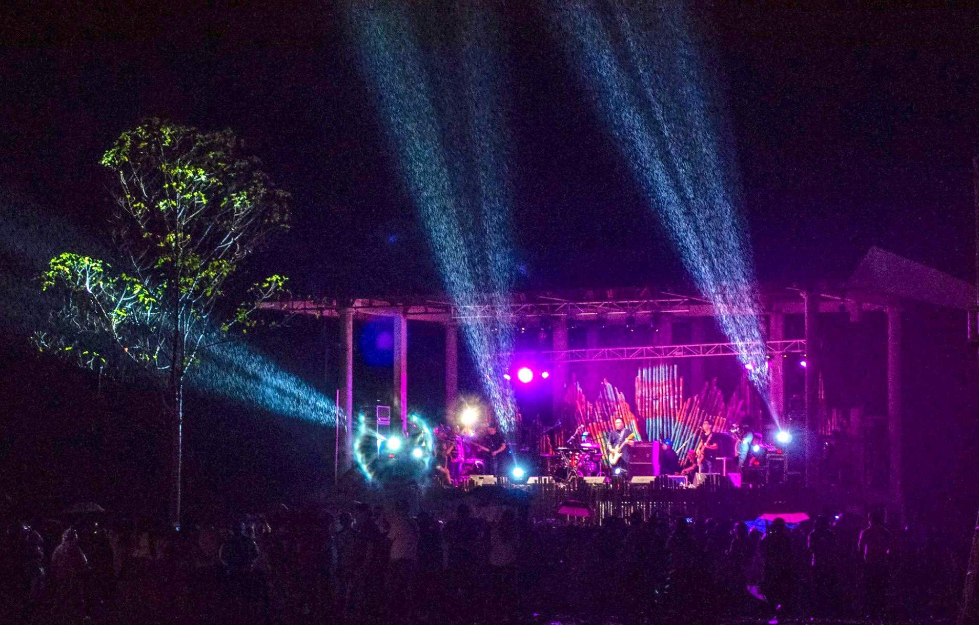 The main stage at night, lit in purple with beams of light over the trees